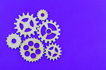Wooden gears of different sizes on a purple background with a copy space. The concept of successful teamwork. New ideas and technologies.