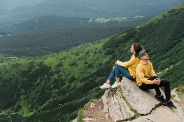 Foto op Canvas Inspirational landscape. Love in the mountains. Happy couple in love sits on the edge of the cliff back to back on the big stone with an amazing mountains view on the background © Kateryna