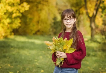 Fotobehang Een mooi meisje in een rode trui houdt herfstbladeren vast. Schattig meisje poseert in het herfstbos © Albert Ziganshin