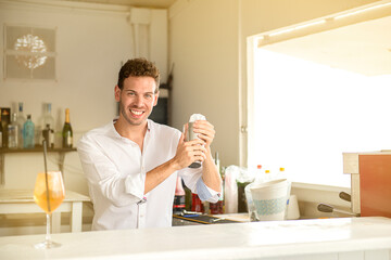 young barman preparing cocktail in beach bar