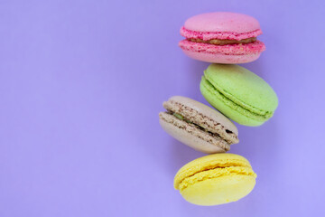 Four yellow, pink, brown and pink biscuit one above the other on violet background with copy space. Traditional french patisserie, top view