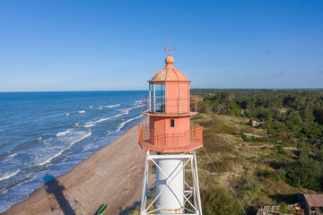 Fototapeta na wymiar Aerial view of lighthouse with red top and white base. Blue sky and sea. Pape lighthouse