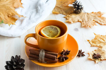 cup with hot tea and lemon, autumn leaves on the wooden background. Seasonal mood and relaxing concept