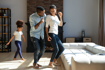 Full length loving young couple with small kid daughter dancing together in modern living room ,...