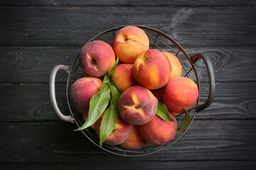 Fresh sweet peaches in metal basket on black wooden table, top view