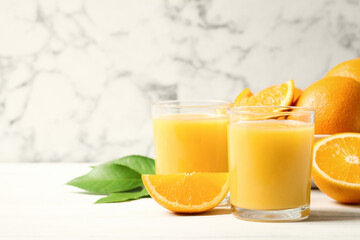 Glasses of orange juice and fresh fruits on white table. Space for text