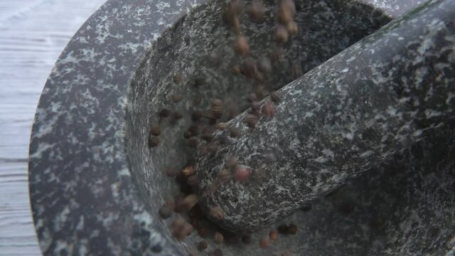 Black peppercorns are falling into the grey stone mortar in slow motion