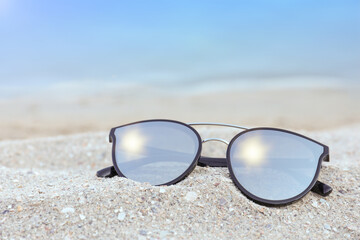 Fototapeta na wymiar Stylish sunglasses on sandy beach near sea
