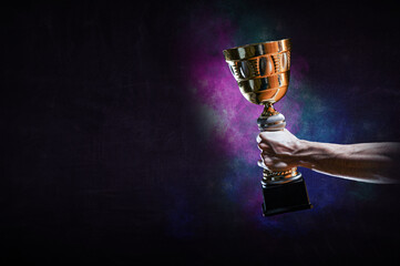 Hand holding up a gold trophy cup against dark background