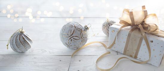Decorative gift box with golden bow and white christmas balls on bright vintage wood. Christmas background with festive bokeh. Close-up with short depth of field and space for text.
