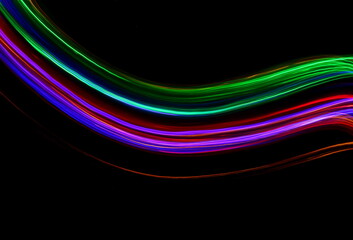 Long exposure photograph of neon multi colour in an abstract swirl, parallel lines pattern against a black background. Light painting photography.