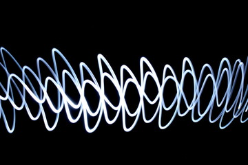 Long exposure photograph of vibrant white colour in an abstract swirl, parallel lines pattern against a black background. Light painting photography.