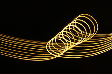 Long exposure photograph of neon gold colour in an abstract swirl, parallel lines pattern against a black background. Light painting photography.