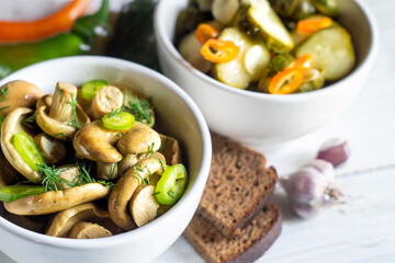 Salted milk mushrooms and pickled cucumbers in bowls on a white wooden table