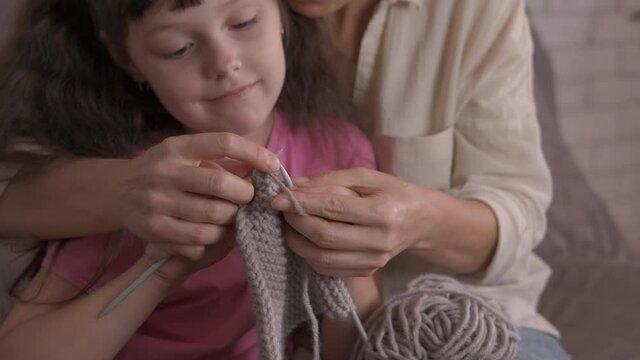 Teaching to knit. A good looking mother teach her smiling little girl to knit.
