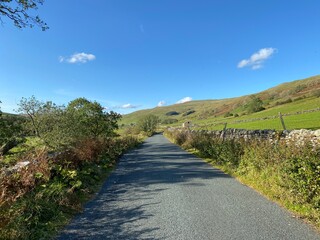 Country road, near Halton Gill, with a farm building, dry stone walls, and hills in the distance 
