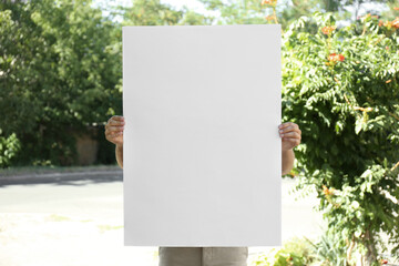 Man holding white empty poster outdoors. Space for design
