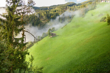Almhütte im Morgennebel am Berghang in den Alpen