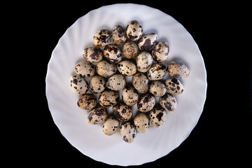 Quail eggs arranged in a white plate, on a black background	