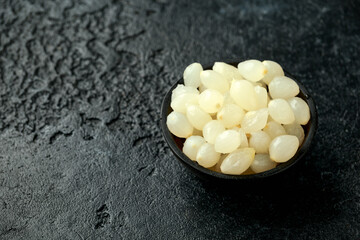 Pickled Cocktail Onions in wooden bowl on rustic black background