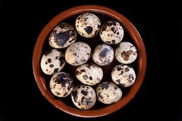 Quail eggs arranged in a small circular earthen dish, on a black background	