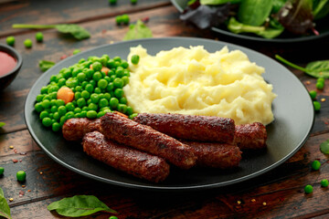 Vegetarian vegan sausages with mashed potato and green peas in black plate