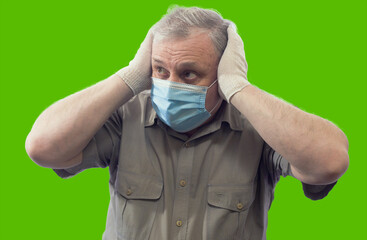 Man in short sleeved shirt, medical mask and gloves anxiously grabbed his head, portrait isolated on green background.