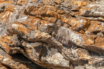 Background texture of rock or schist formations on the cliff near coast. Orange lichens on the gray stone.
