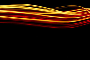 Long exposure photograph of neon red and gold colour in an abstract swirl, parallel lines pattern against a black background. Light painting photography.