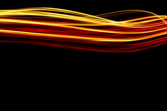 Long exposure photograph of neon red and gold colour in an abstract swirl, parallel lines pattern against a black background. Light painting photography.