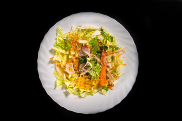 Mixed salad, fresh, light and colorful, in a white plate, on a black background	