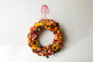 Beautiful autumnal wreath with flowers, berries and fruits hanging on white wall. Space for text