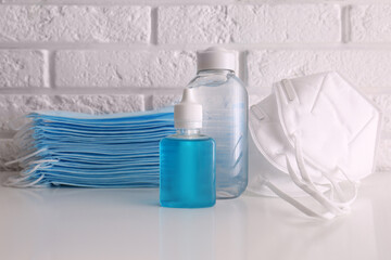 Hand sanitizers and respiratory masks on table near white brick wall. Protective essentials during COVID-19 pandemic