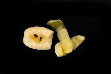 Piece of cut and peeled apple, peels and seeds, on black background	
