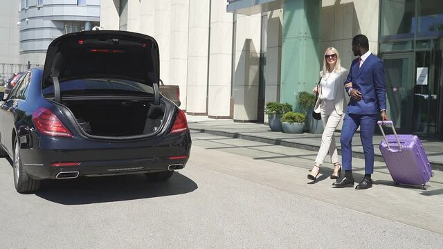Multiethnic couple leave hotel together, young man and woman in formal wear heading to the car.