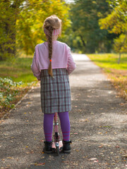 Obraz premium Child riding on kickscooter. Blonde cute girl in plaid dress on scooter on asphalt road. Autumn active lifestyle leisure, physical training on sports stadium. Happy childhood street photo with bokeh.