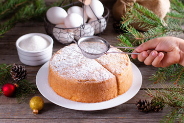 Homemade sponge cake with powdered sugar on a white plate on a wooden table. New Year and Christmas sponge cake on white plate so soft and delicious with ingredients: eggs, flour, milk