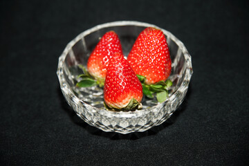 Trio of strawberries in a crystal cup, on a black background	