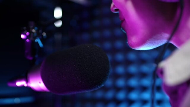 Beautiful young girl dj speaks into microphone, records podcast or morning news show for radio. Close up of podcast presenter or DJ talking on the microphone. Wears professional headphones