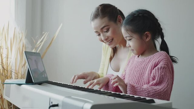 Mother Asian is teaching daughter to play an electric piano in house. Family activities that happy together. Online music school business. Concept video conference