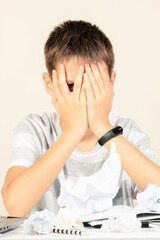 Kid covering his face with hands and peering out with one eye between fingers. Sad boy have learning problem with homework