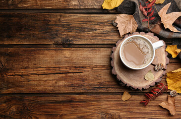 Flat lay composition with cup of hot drink, plaid and autumn leaves on wooden background, space for text. Cozy atmosphere