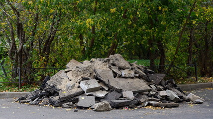 A pile of pieces of broken asphalt pavement on the edge of a green Park