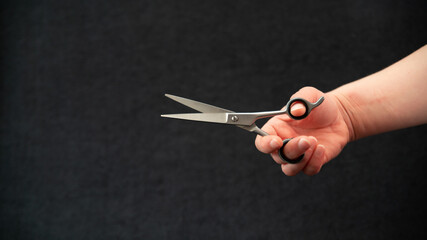 Close-up of a hand holding a pair of hairdressing scissors, on a black background	
