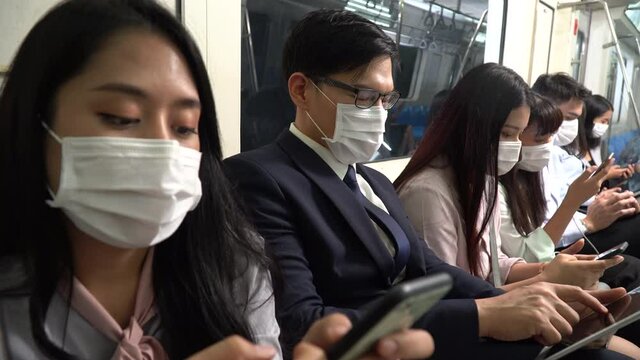 asian business  people wearing surgical mask using smartphone sitting in subway . new normal during  Coronavirus pandemic or Covid-19 outbreak concept