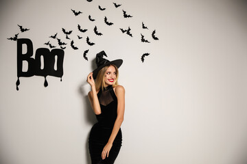 Woman in witch hat posing near white wall decorated for Halloween