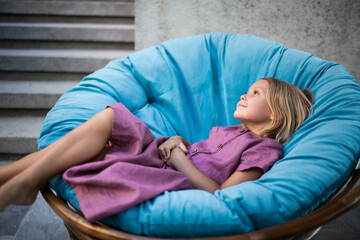 Beautiful girl in lilac linen dress is chilling on the round blue soft armchair
