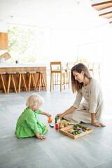 Naklejka premium Mother is playing wooden toys with her little baby daughter