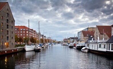 White moored motor boats in a channel and european houses on the embankment against cloudy sky in Copenhagen, Denmark.