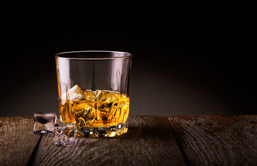 Crystal glass of whiskey with ice cubes on wooden table.